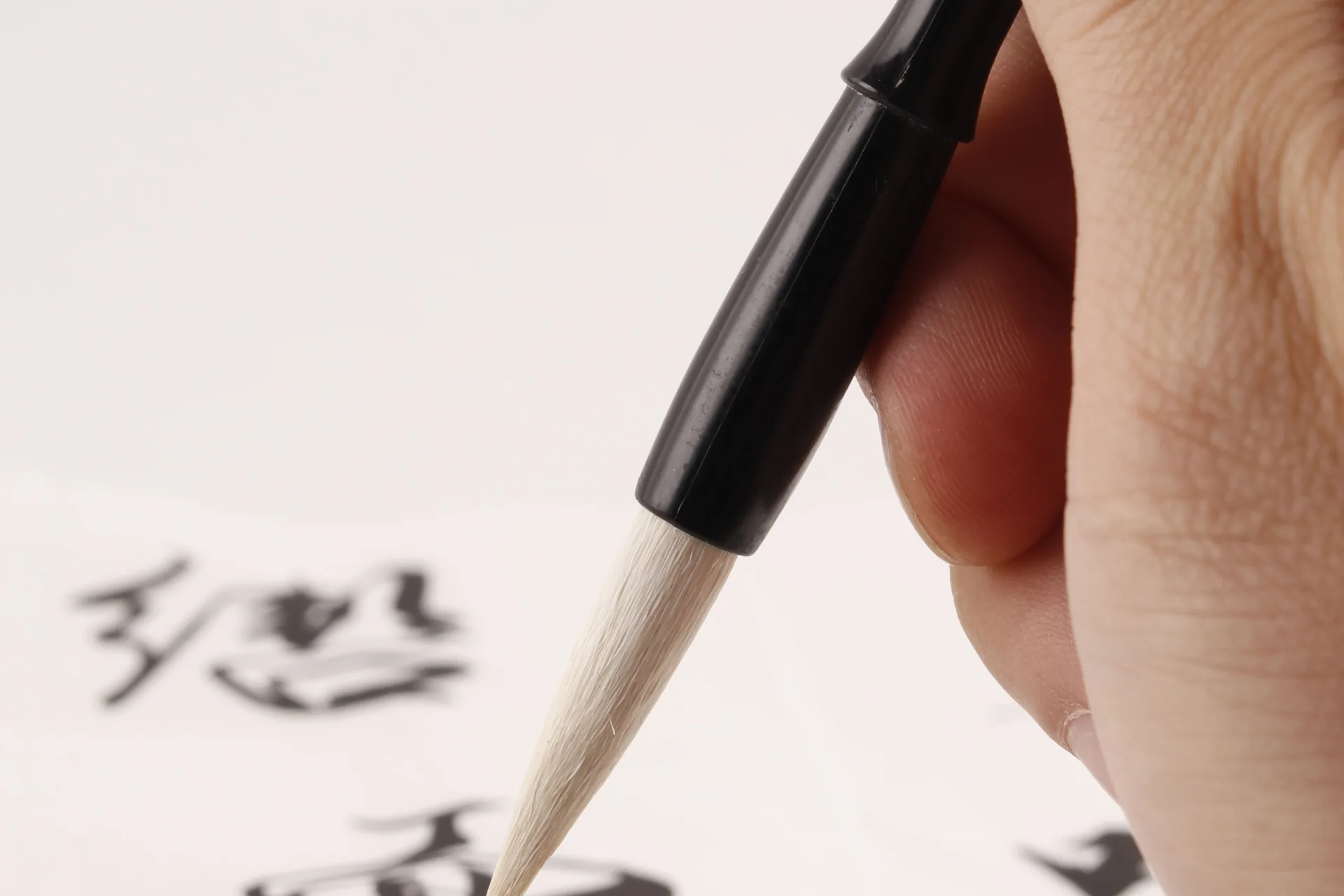 Mano escribiendo caracteres japoneses con un pincel de caligrafía sobre papel blanco