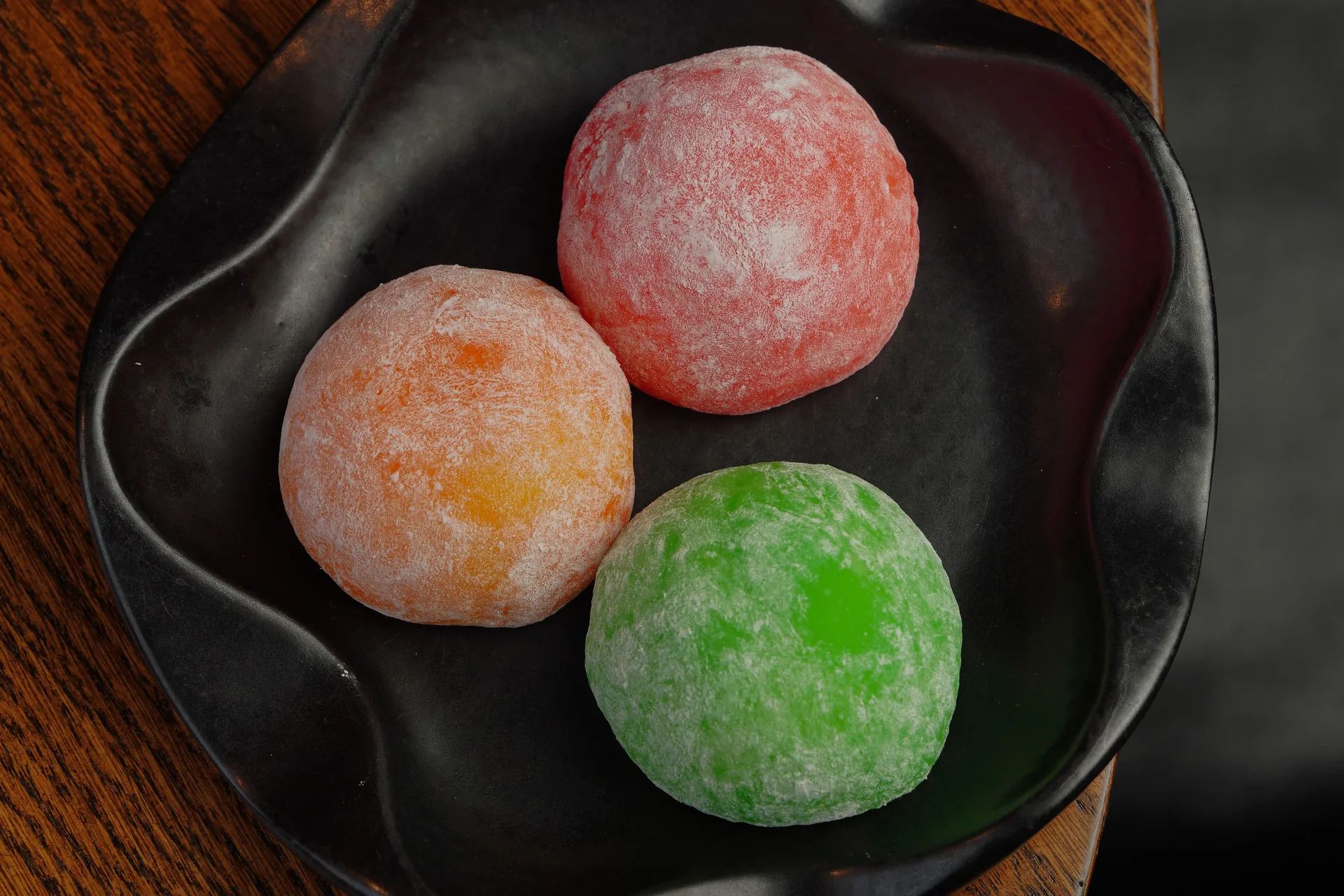 Mochi: qué es, cómo se hace y los tipos que tienes que probar en Japón 2026 Tres mochis daifuku de colores sobre un plato negro