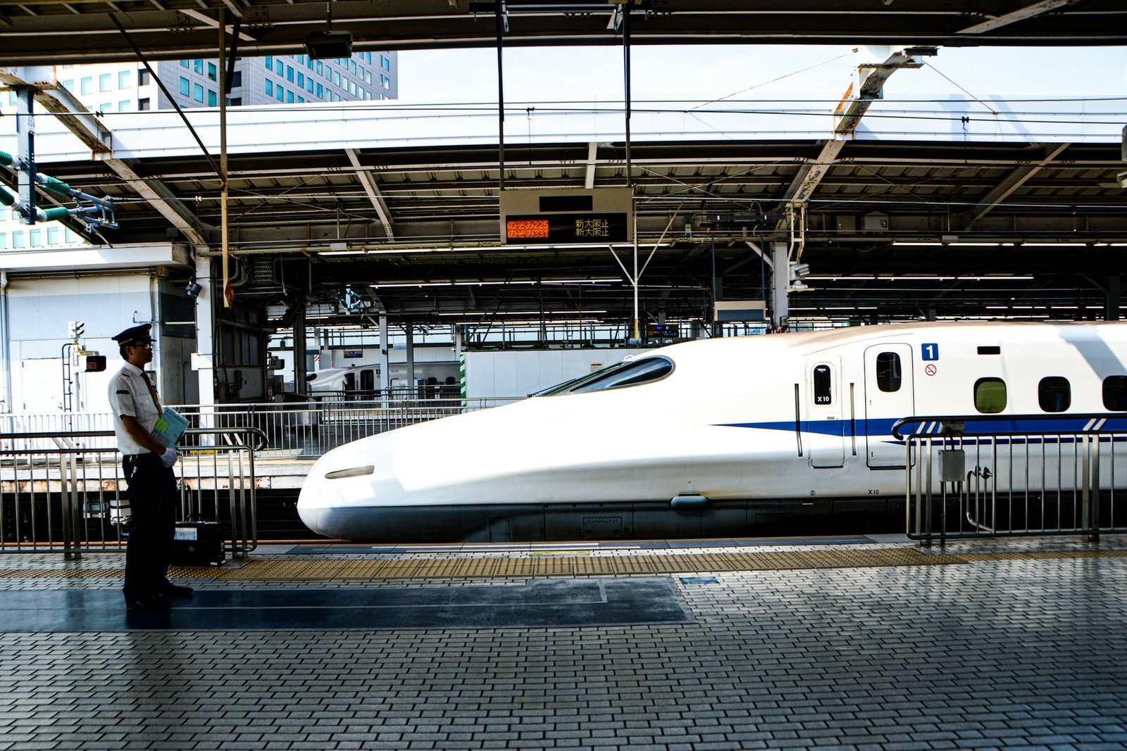 Shinkansen serie N700 detenido en un andén con un empleado de JR vigilando la vía